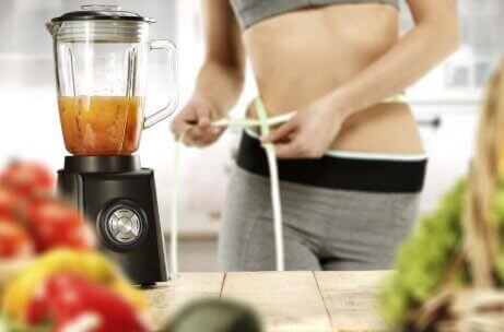 Vrouw meet haar taille op terwijl ze een smoothie maakt